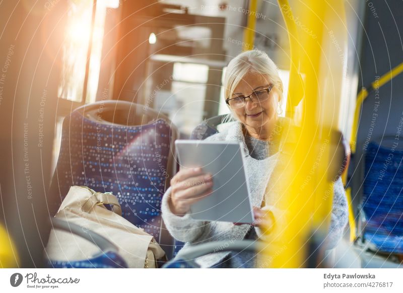 Ältere Frau benutzt Tablet, während sie mit dem öffentlichen Bus fährt Senior Senioren Rentnerin Rentnerinnen lässig im Freien eine Person