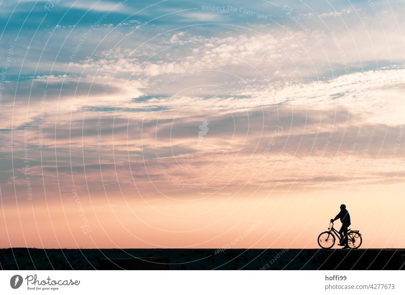 ein Mann wartet in der Abendsonne auf seinem Fahrrad am Deich Sonnenuntergang Sommerurlaub Insel Warten eine Person Sonnenuntergangshimmel Strand Minimalismus