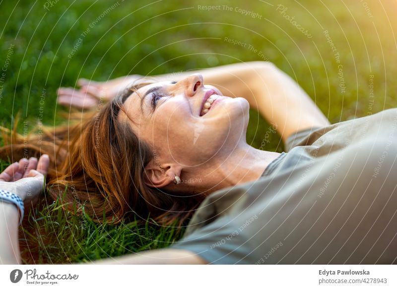 Sorglose Frau auf dem Gras in der Sonne liegend hoher Winkel Tagträumen oben träumend ruhen grün Lügen Rasen Wiese Park Natur Frühling rote Haare Rotschopf