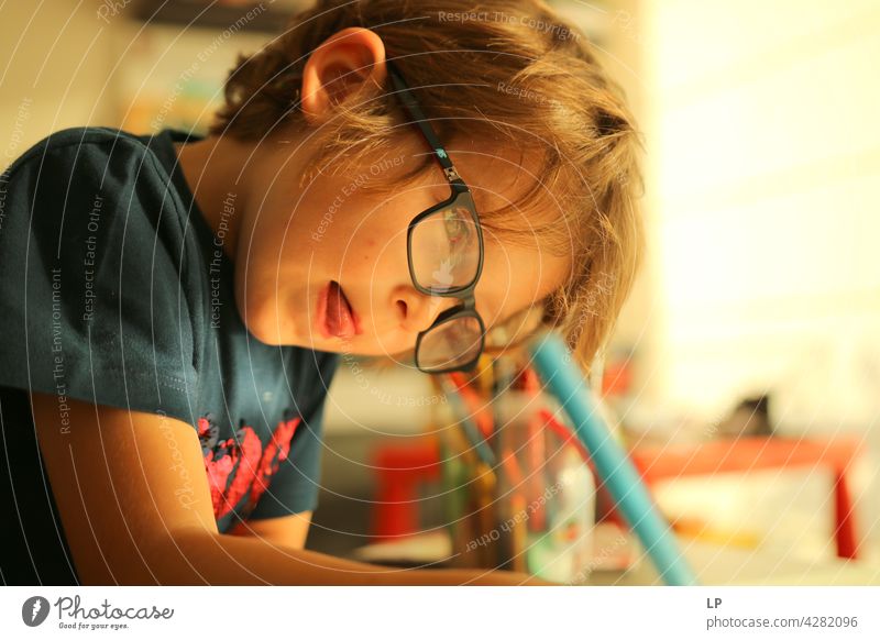 Kind trägt Brille und schreibt, während es sehr konzentriert ist Oberkörper Porträt Muster talentiert zeichnen Zeichenutensilien Abenteuer Lebensfreude Freude