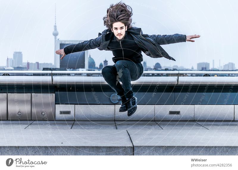 Der dynamische junge Mann mit den langen Haaren landet auf dem Dach einer Großstadt springen energisch schwungvoll oben Reichstag Parkour Panorama mutig