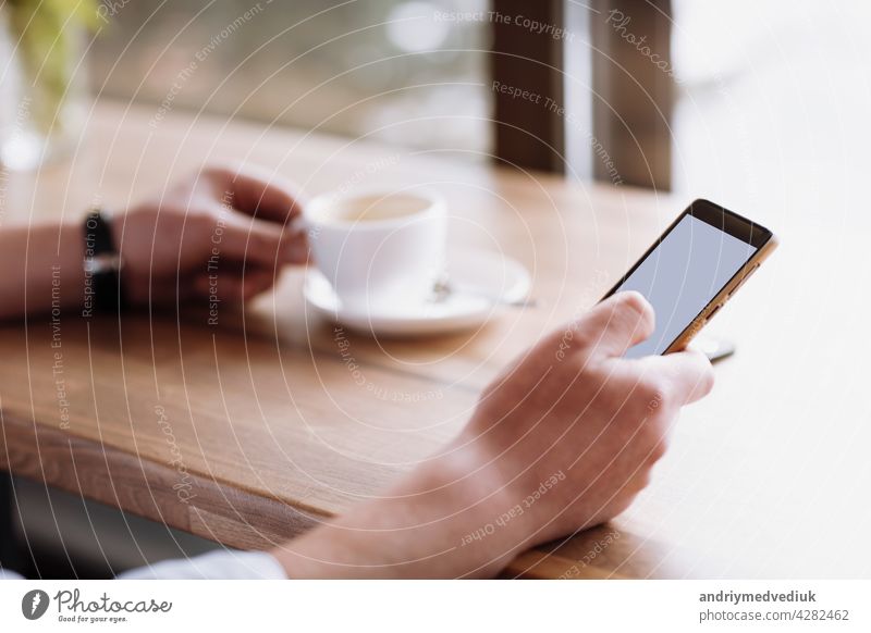 Geschäftsmann Hand hält ein Telefon mit isolierten Bildschirm gegen moke up und trinken Kaffee im Coffee Shop verschwommen Kaffeetasse Hintergrund, Mock up Konzept