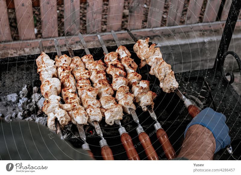 Der Chefkoch bereitet Hähnchen-Schaschlik zu. Türkisches Streetfood. Fleisch gekocht über einem Feuer, BBQ-Party im Hinterhof. Männliche Hände in Handschuhen halten Stahlspieße mit leckeren Hähnchen-Schaschliks