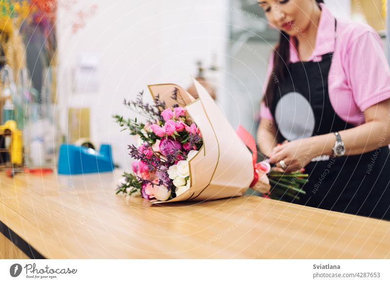 Nahaufnahme eines schönen Blumenstraußes, den ein Blumenmädchen in Geschenkpapier einwickelt. Blumengeschäft, Arbeit mit Blumen, Blumenstrauß Blumenhändler