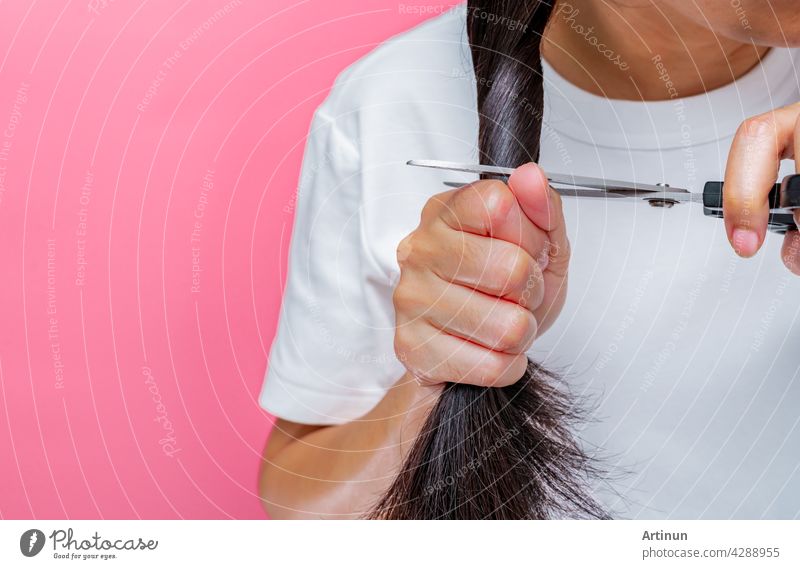 Frauen schneiden beschädigte und trockene Haare. Asiatische Frau Schneiden von Haaren mit Schere für die Spende an Krebspatienten. Haarspende für Brustkrebs Person. Frau mit schwarzen langen Haaren auf rosa Hintergrund.