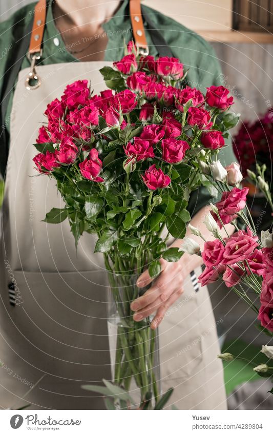Eine Blumenhändlerin in einer Schürze hält eine Vase mit Rosen. Menschen bei der Arbeit. Florist Arbeitsplatz. Blumenladen. Kleines Geschäftskonzept. Nahaufnahme. Vertikale Aufnahme