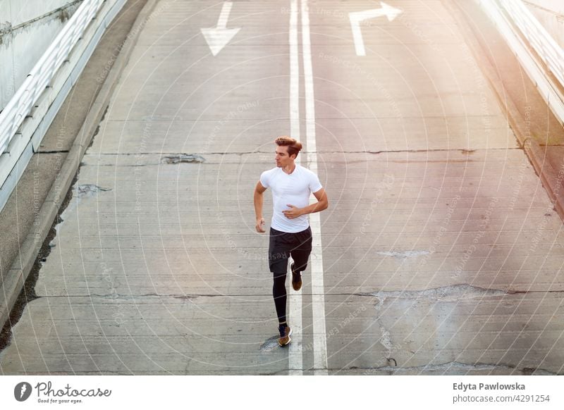 Junger Mann läuft auf Parkebene in der Stadt bei Sonnenuntergang Jogger Läufer Joggen rennen Menschen jung männlich Energie Übung Bekleidung trainiert. Fitness