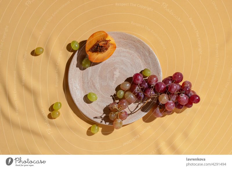 Geschnittener frischer Pfirsich und Traube auf selbstgemachtem Keramikteller auf gelber Tischdecke, Früchte Catering Trauben Diät Vitamin Sommer Snack