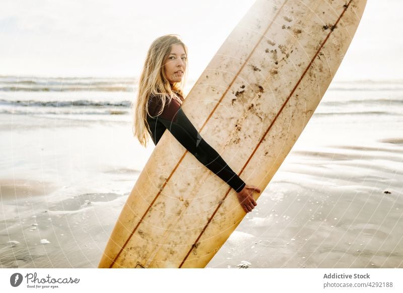 Weibliche Surferin am Strand mit Surfbrett stehend Frau Natur Sonnenuntergang winken im Freien Neoprenanzug Meeresküste Brandung Sportlerin MEER Surfen Hobby
