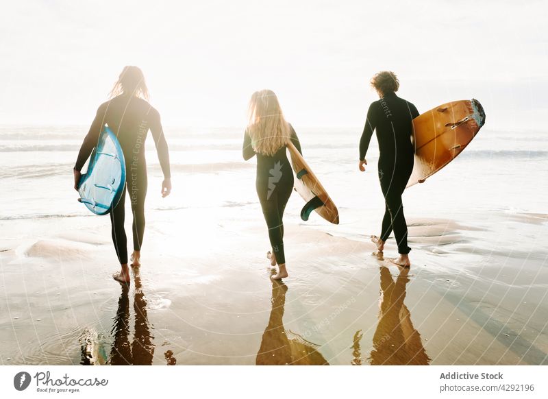 Anonyme Surferfreunde am Strand mit Surfbrettern Freunde Natur Sonnenuntergang winken im Freien Neoprenanzug Meeresküste Zusammensein Brandung MEER Surfen Hobby