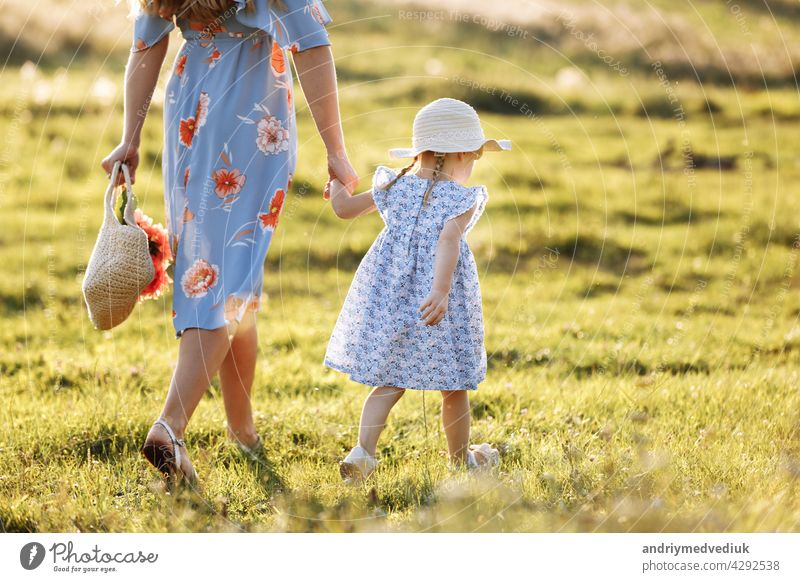 Junge Mutter, die mit ihrer kleinen Tochter auf der grünen Wiese spazieren geht. Familienurlaub im Garten. Portrait Mama mit Kind zusammen auf Natur. Mutter, kleine Tochter im Freien. Alles Gute zum Muttertag. Nahaufnahme