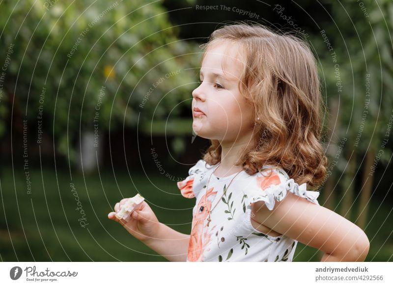 Lustige Kind Mädchen essen Sandwich im Freien. Hat Spaß. Schaut in die Kamera. Posieren über Natur Hintergrund. Gesundes Essen. Kindheit. Lebensmittel Glück