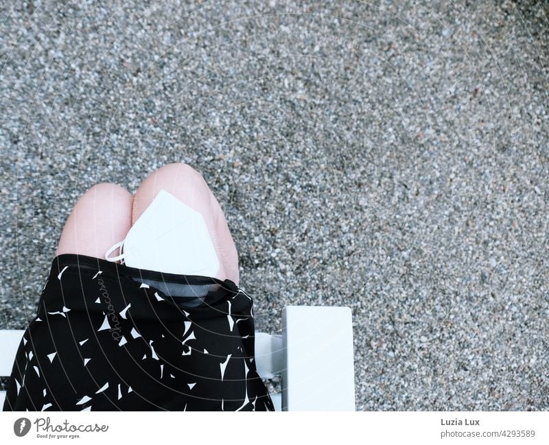 Sommer, Coronazeit: Frau im Kleid sitzt im Park, eine weiße Maske auf ihrem Knie ist halb unter den Rock gerutscht Frau mit Maske Gesichtsmaske Lifestyle