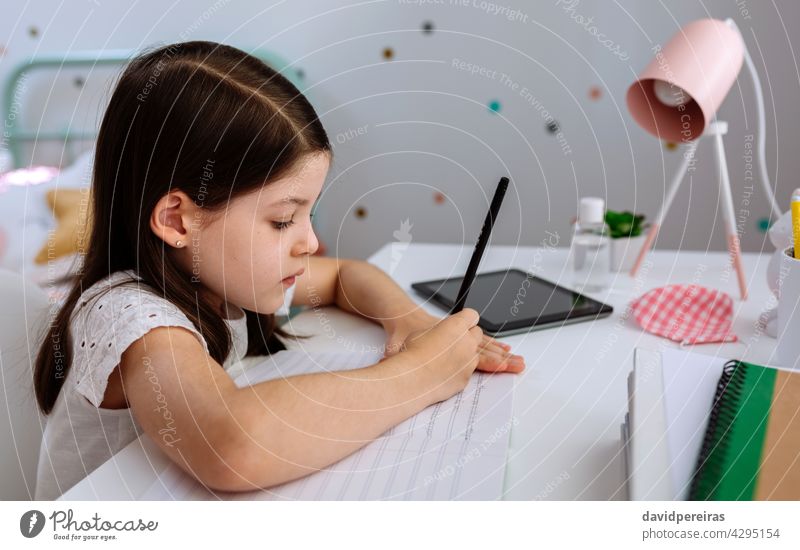 Mädchen studiert zu Hause mit Maske auf dem Tisch schreibend Schreibtisch Homeschooling Schule zu Hause Coronavirus Seuche Desinfektionsmittel heimwärts