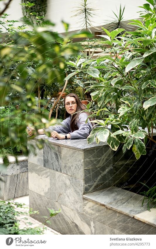 Junge Brünette Mädchen verwendet Handy Texting auf Smartphones Nachrichten macht Selfie beim Sitzen im botanischen Garten der Stadtbibliothek Frau Texten