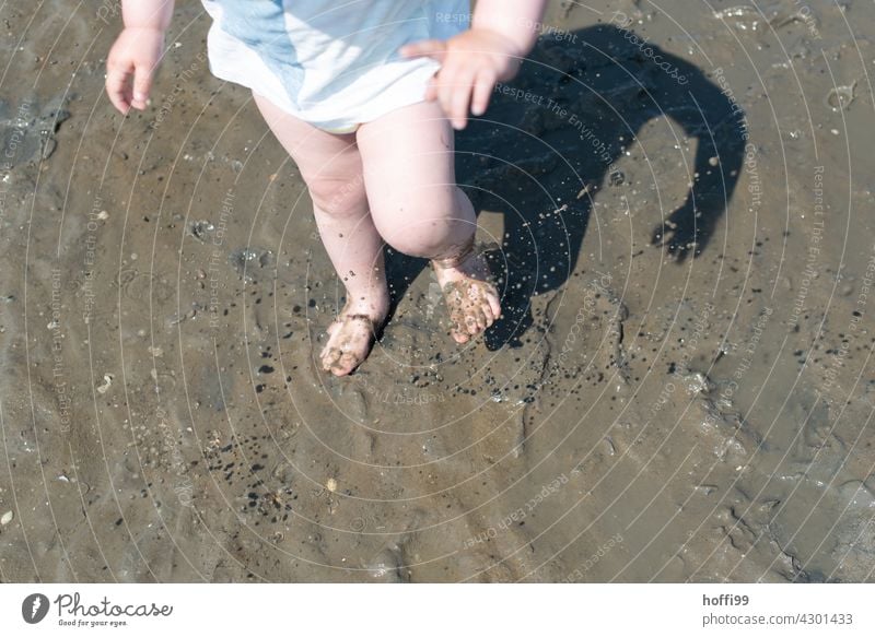 das kleine Kind spielt und stampft im Watt in eine Pfütze Kinderfüße matschig Schlick Wattwandern Matsch dreckig Wasser nass Nordsee Ebbe Schlamm Beine