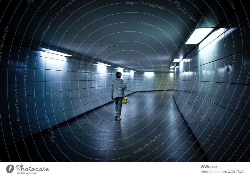 Eine Frau läuft allein durch den kalt erleuchteten Übergang einer U-Bahn-Station Passantin einsam Bahnhof öffentlich Tunnel laufen gehen unsicher Verkehr