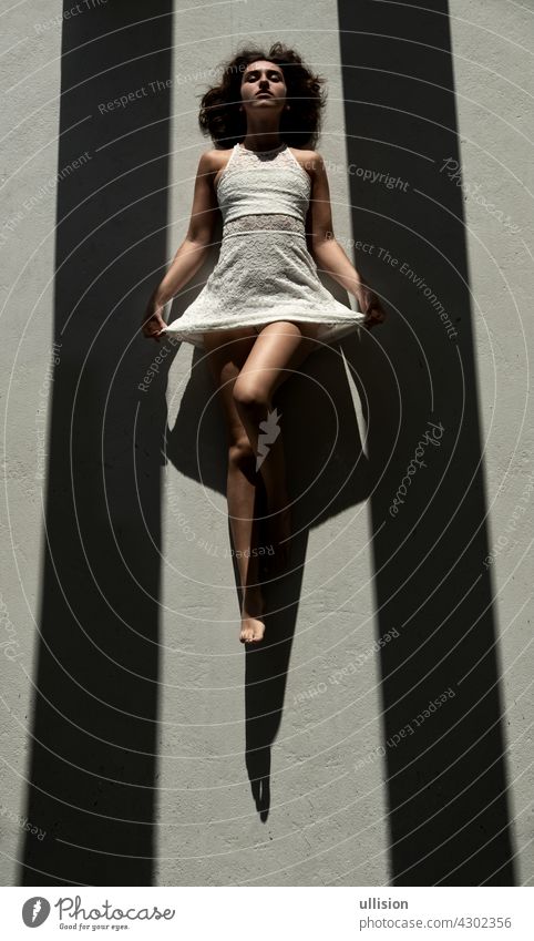 junge sexy Frau liegt zwischen zwei schwarzen Schattenstreifen auf dem Boden in der Sonne und wirft einen starken Schatten Kleid dunkel weiß geheimnisvoll