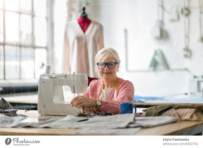 Senior-Modedesignerin an der Nähmaschine in ihrer Werkstatt Stoff Gewebe Material Nähen Designer Damenschneiderin Näherin Schneider Bekleidung im Innenbereich