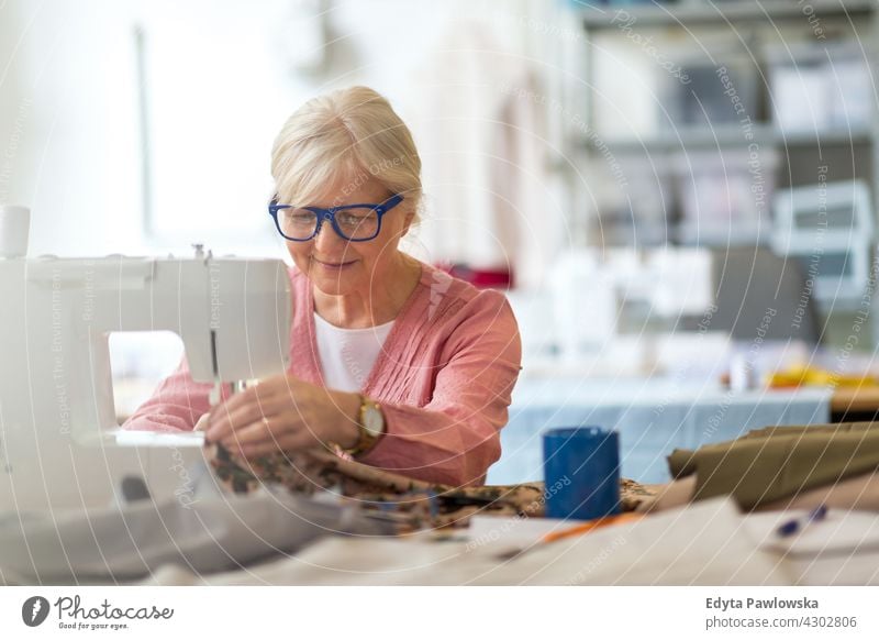 Ältere Frau an einer Nähmaschine Stoff Gewebe Material Nähen Mode Designer Damenschneiderin Näherin Schneider Bekleidung im Innenbereich Mechaniker Besitzer