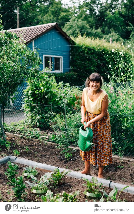 Frau gießt im Schrebergarten die Gemüsebeete mit einer Gießkanne Garten gießen Gartenarbeit Natur Sommer Gärtnerin bunt fröhlich lachen gute Laune Pflanzen