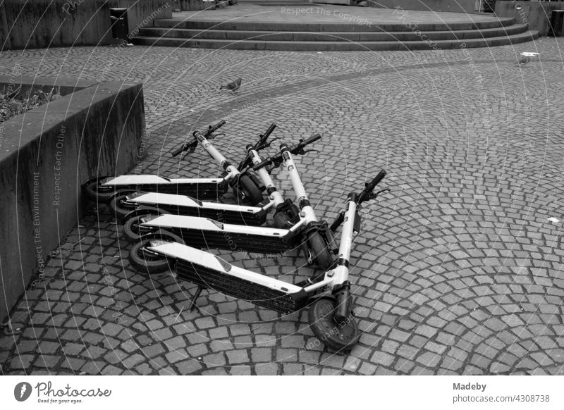 Umgestürzte E-Scooter für Touristen auf Kopfsteinpflaster in der Innenstadt von Frankfurt am Main in Hessen, fotografiert in neorealistischem Schwarzweiß Roller
