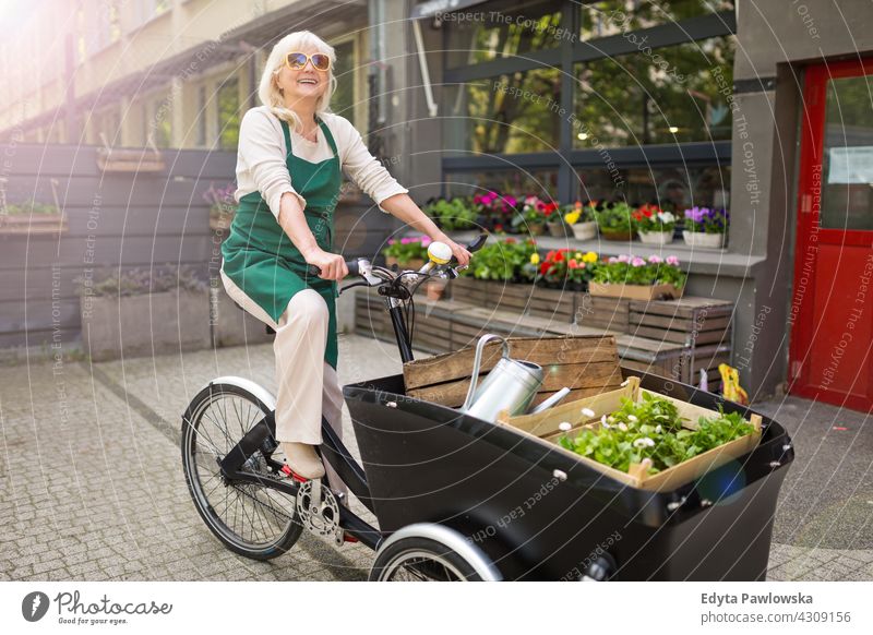 Glückliche Besitzerin eines Blumenladens mit Lastenfahrrad Fahrrad Fahrradfahren Verkehr Pendeln Lastenrad Versand Blumenhändler Menschen Erwachsener Senior