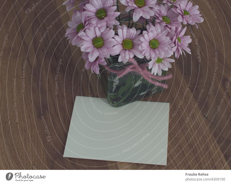 Unbeschriebene Karte unter eine Blumenvase geschoben auf einem Holztisch Grußkarte Nachricht Notiz Glückwünsche Danke Abschied Liebe Geburtstag Muttertag