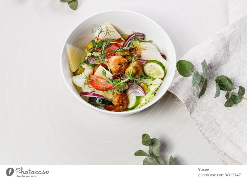 Close-up leckeren Sommersalat mit frischem Gemüse und Meeresfrüchten auf einem weißen Hintergrund. Gemüse der Saison, Garnelen und Ziegenkäse. Gesunde mediterrane Naturkost. Lebensmittel-Fotografie. Kopierraum