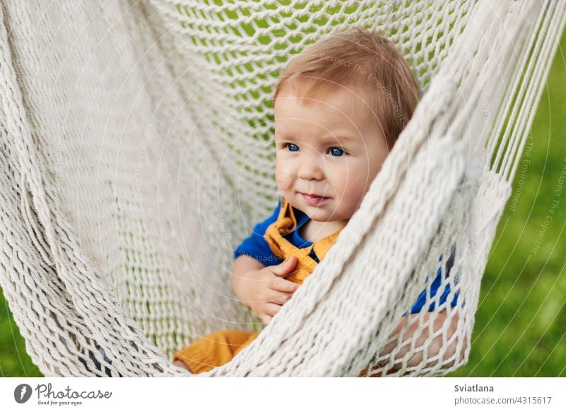 Ein kleiner Junge sitzt in einer Hängematte an einem Sommertag im Garten Baby Kleinkind Kind Sonne grün Natur Sommerzeit Sonnenbad sich[Akk] entspannen