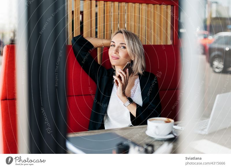 Ein attraktives Mädchen spricht mit einem Mobiltelefon und lächelt, sitzt allein in einem Café Telefon sprechend Frau Sitzen Tablette Geschäftsfrau Business