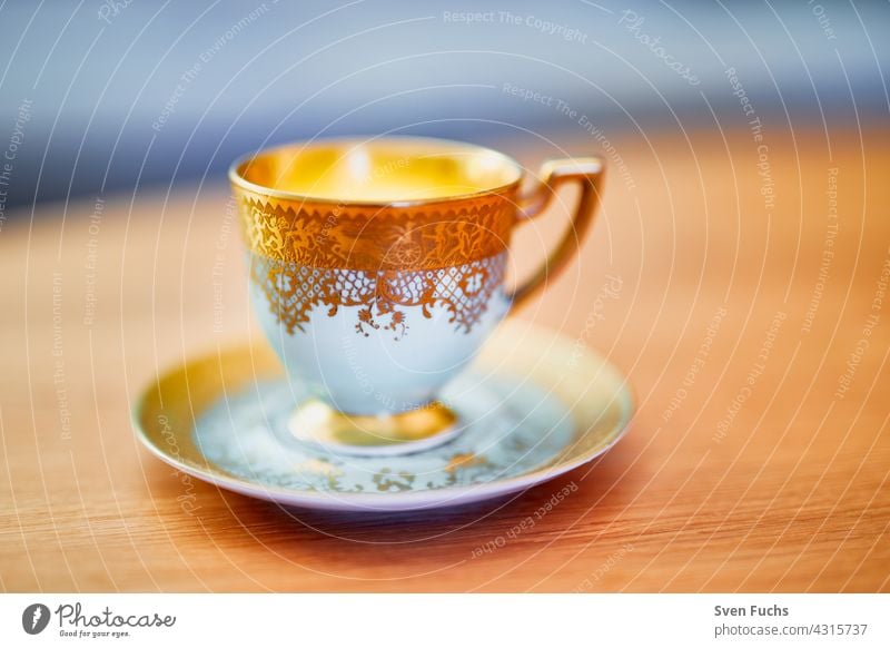 Kaffeetasse und Untertasse mit Goldverzierung stehen auf einem Holztisch kaffeetasse goldrand geschirr mokka porzellan altmodisch edel festlich untertasse