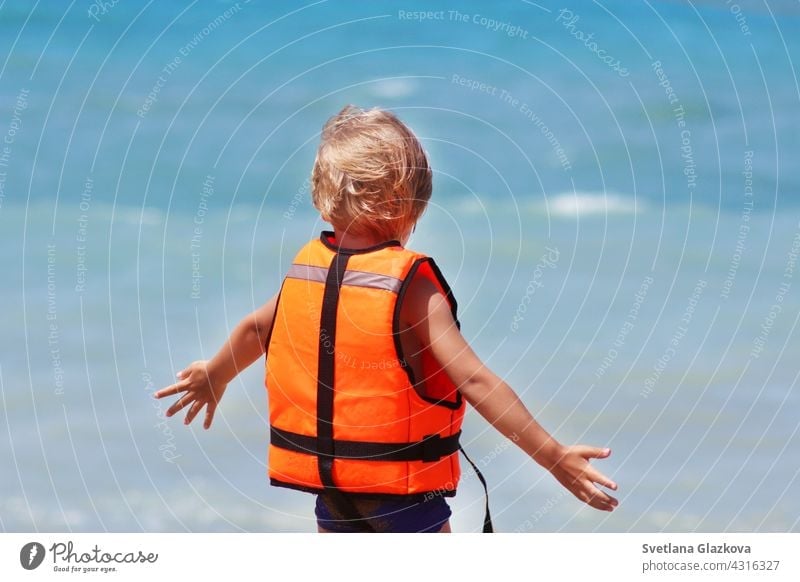 Sicherheit des Lebens Konzept. Kleine kaukasische Junge verwendet eine Schwimmweste auf einem Sommerstrand vor dem Hintergrund der Meereswellen.