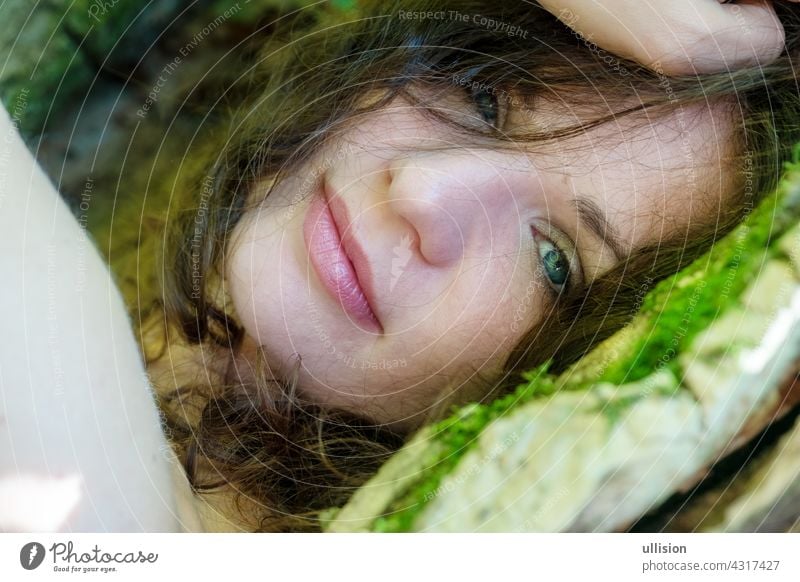 Porträt einer schönen dunkelhaarigen jungen sexy Frau liegt glücklich zufrieden im Bett von Moos im Wald mit in einem alten Weidenbaum mit nackten Schultern und tiefen Frieden in das Lächeln