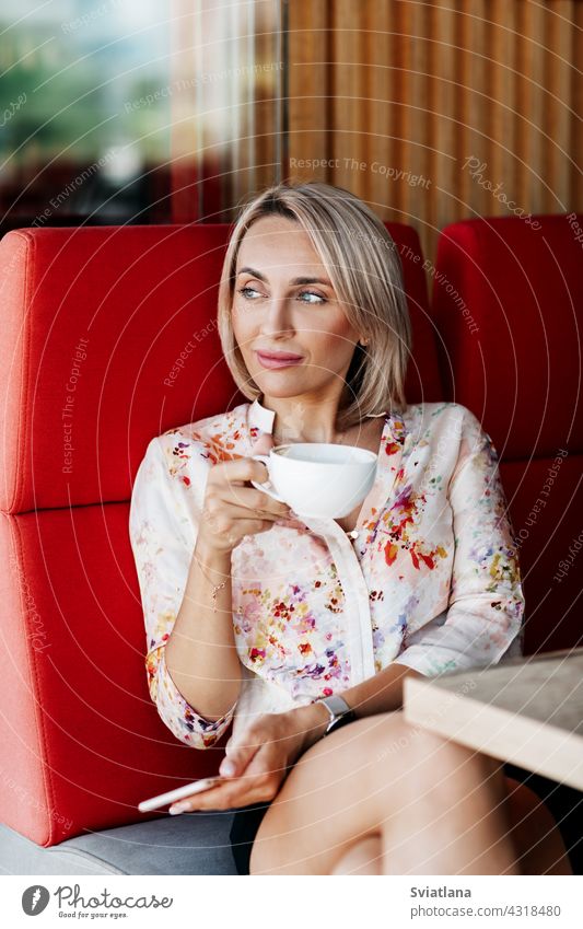 Ein schönes Mädchen trinkt Kaffee in einem Café und schaut nachdenklich in die Ferne Frau Mobile benutzend trinken Nachricht Beteiligung Menschen