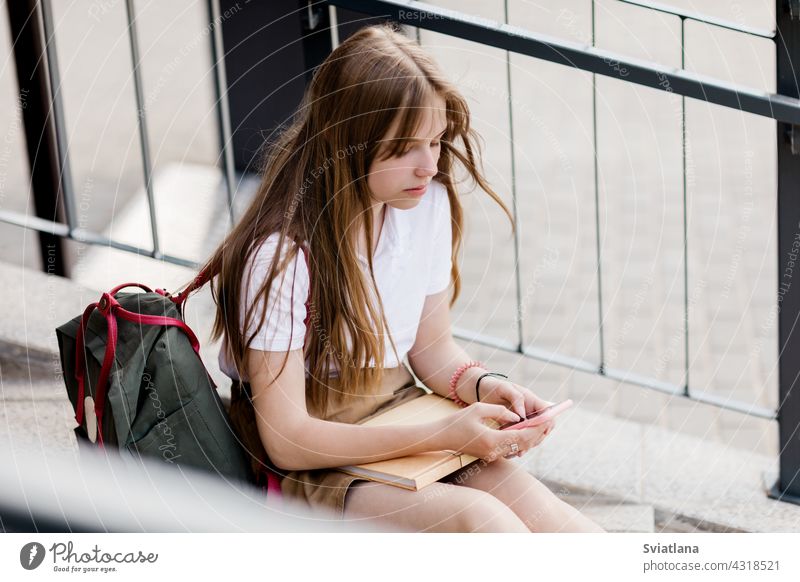 Nettes Mädchen sitzt auf der Treppe außerhalb des Campus nach College-Klasse und plaudert mit ihren Freunden Teenager Sitzen Telefon benutzend Rucksack