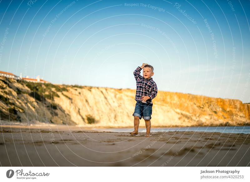 Kleiner Junge wirft Steine am Strand bei Sonnenuntergang spielen Kleinkind Textfreiraum Sagres Portugal Barfuß Sohn horizontal Baby sonnig laufen Seeküste