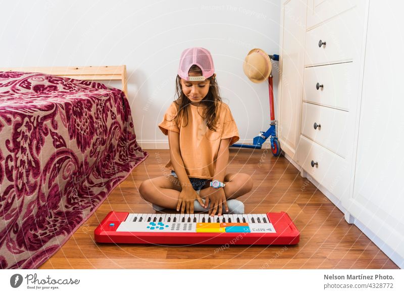 Kleine hispanische Mädchen trägt eine rosa Tasse spielen in einem roten Klavier in ihrem Schlafzimmer Pianist Person Akkord Klassik Finger Rhythmus kreieren