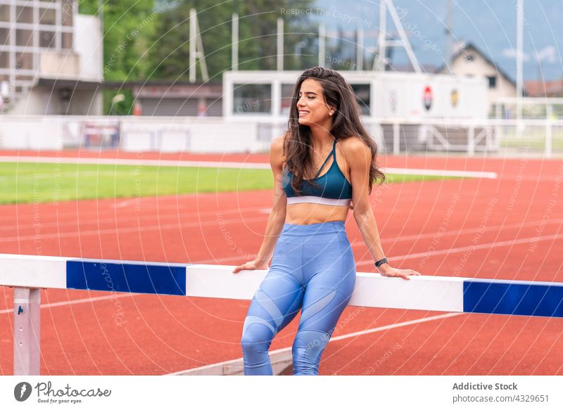 Glückliche Sportlerin ruht sich in der Nähe der Hürde auf der Stadionbahn aus Athlet Lächeln ruhen Bahn Pause Sportbekleidung Läufer Frau jung hispanisch