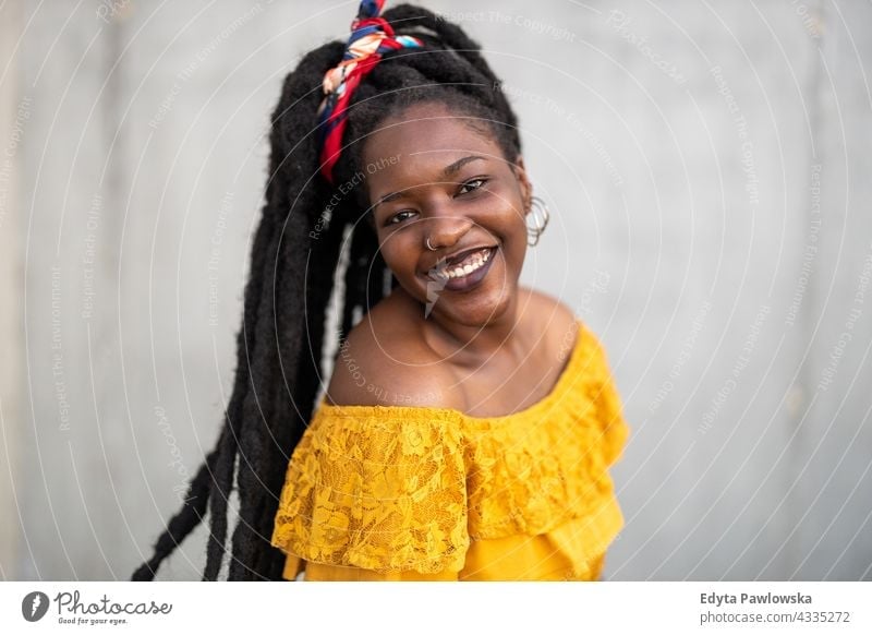 Schöne junge Frau mit Dreadlocks vor einer grauen Wand Rastalocken stolz echte Menschen Stadtleben Afroamerikaner Afrikanisch schwarz Ethnizität sonnig