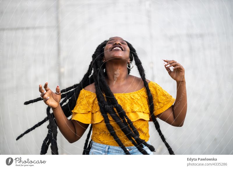 Schöne junge Frau tanzt vor einer grauen Wand Rastalocken stolz echte Menschen Stadtleben Afroamerikaner Afrikanisch schwarz Ethnizität sonnig Sonnenuntergang