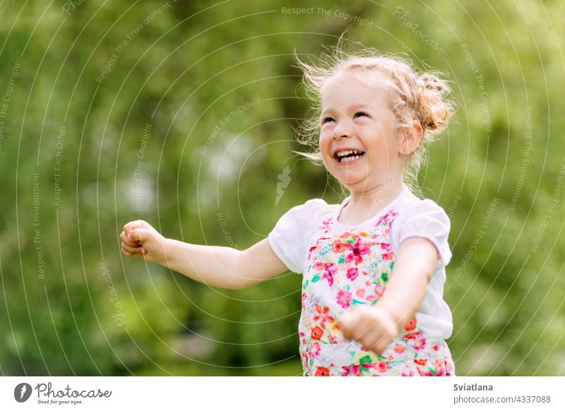 Glückliches lachendes Baby-Mädchen, das in einem Kleefeld läuftEin glückliches lachendes Baby läuft durch den Park oder Garten. Sommer, Sommerzeit, glückliche Tage