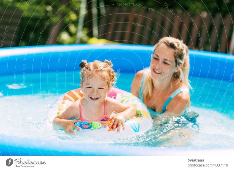 Eine junge Mutter bringt ihrer kleinen Tochter mit Hilfe eines aufblasbaren Kreises das Schwimmen im Pool im Garten bei Mama Badeanzug aufblasbarer Kreis Wasser