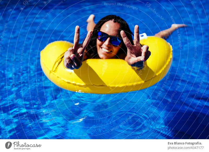 Draufsicht auf glückliche kaukasische Frau entspannt auf gelben Donuts aufblasbare am Pool. machen V-Zeichen mit Händen. Sommerzeit, Urlaub und Lebensstil