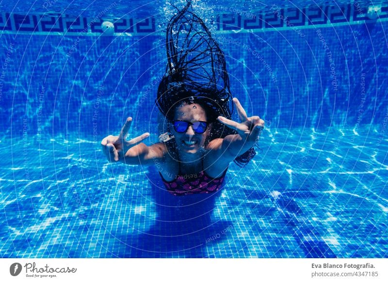 glückliche kaukasische Frau mit Sonnenbrille Tauchen im Schwimmbad. Unterwasser-Ansicht. machen V Zeichen. Sommerzeit und Urlaub Konzept unter Wasser Spaß Liebe