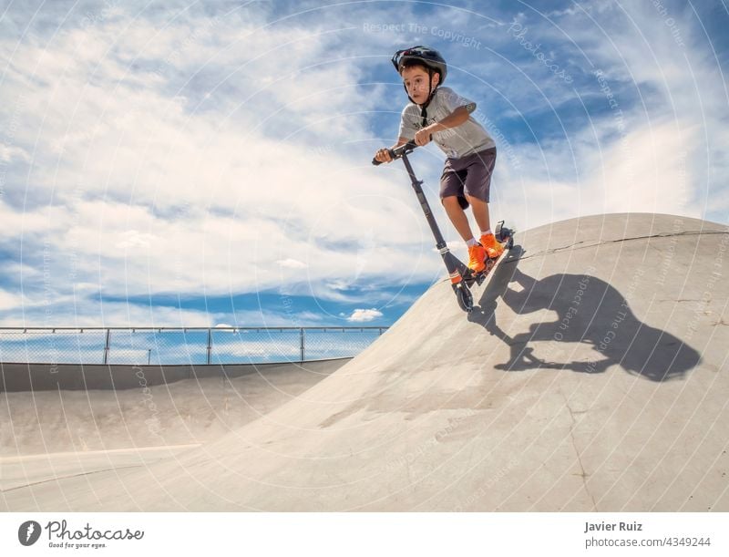 Kind mit Helm fährt an einem sonnigen Sommertag mit einem Roller in einem Skatepark eine Rampe hinunter Tretroller Schlittschuh Skater Junge Skateplatz