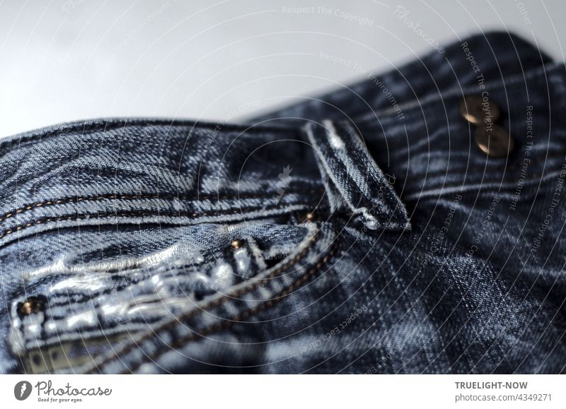 Fast neu, Kult und stylish: Detailaufnahme einer verwaschenen und zerrissenen Bluejeans mit Hosentasche, Gürtelschlaufe und Metallknöpfen Jeans style Mode