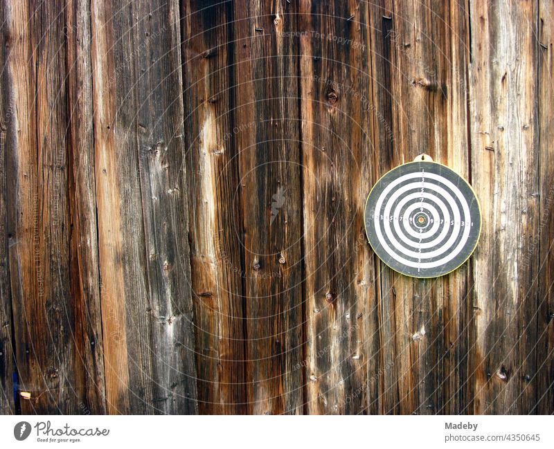 Runde Dartscheibe für das Dartspiel auf dem braunen Holz der Fassade einer alten Scheune auf einem Bauernhof in Rudersau bei Rottenbuch im Kreis Weilheim-Schongau in Oberbayern