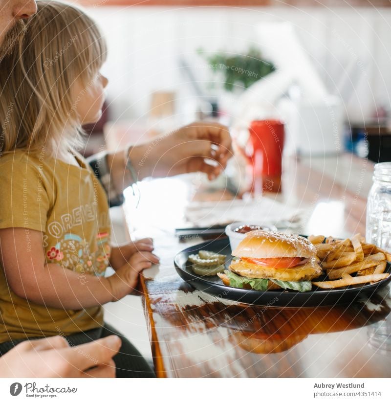 Vater und Tochter essen einen Cheeseburger mit Pommes in einem amerikanischen Diner Amerikaner Hintergrund Barbecue grillen Rindfleisch groß blond Brot Brötchen