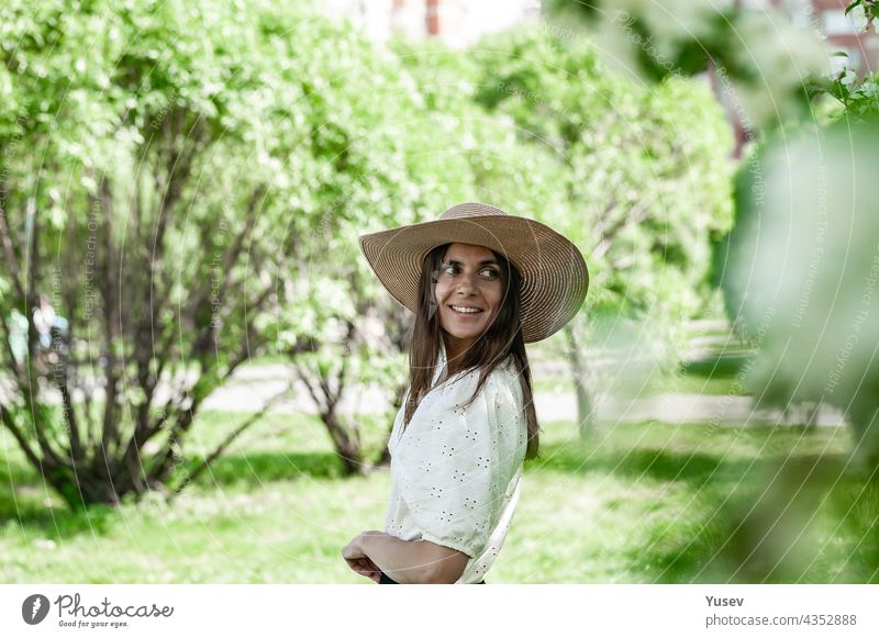 Porträt hübsche und attraktive Frau in einem Strohhut. Junge Frau in auf einem Frühling Park Hintergrund. Nette lächelnd und glücklich junge Frau. Schönes Modell auf der weißen Bluse. Lebensstil